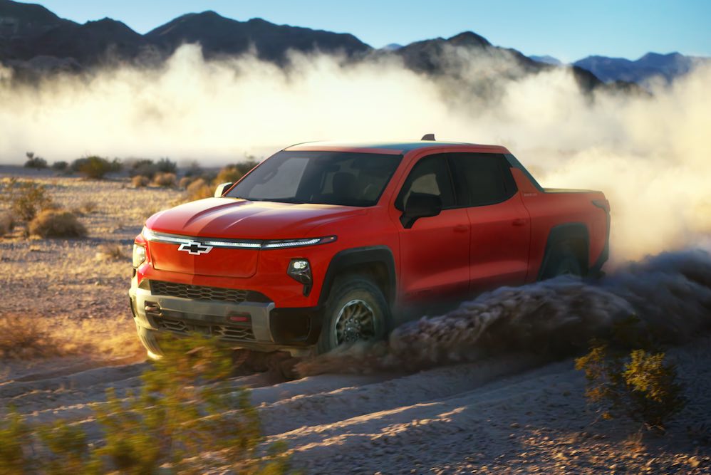 Front 3/4 view of the 2026 Silverado EV Trail Boss in Habanero Orange driving off-road.